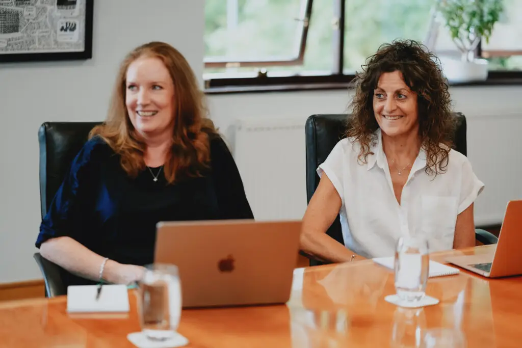 Two Fogwill & Jones employees sat at the table in a meeting room, smiling.