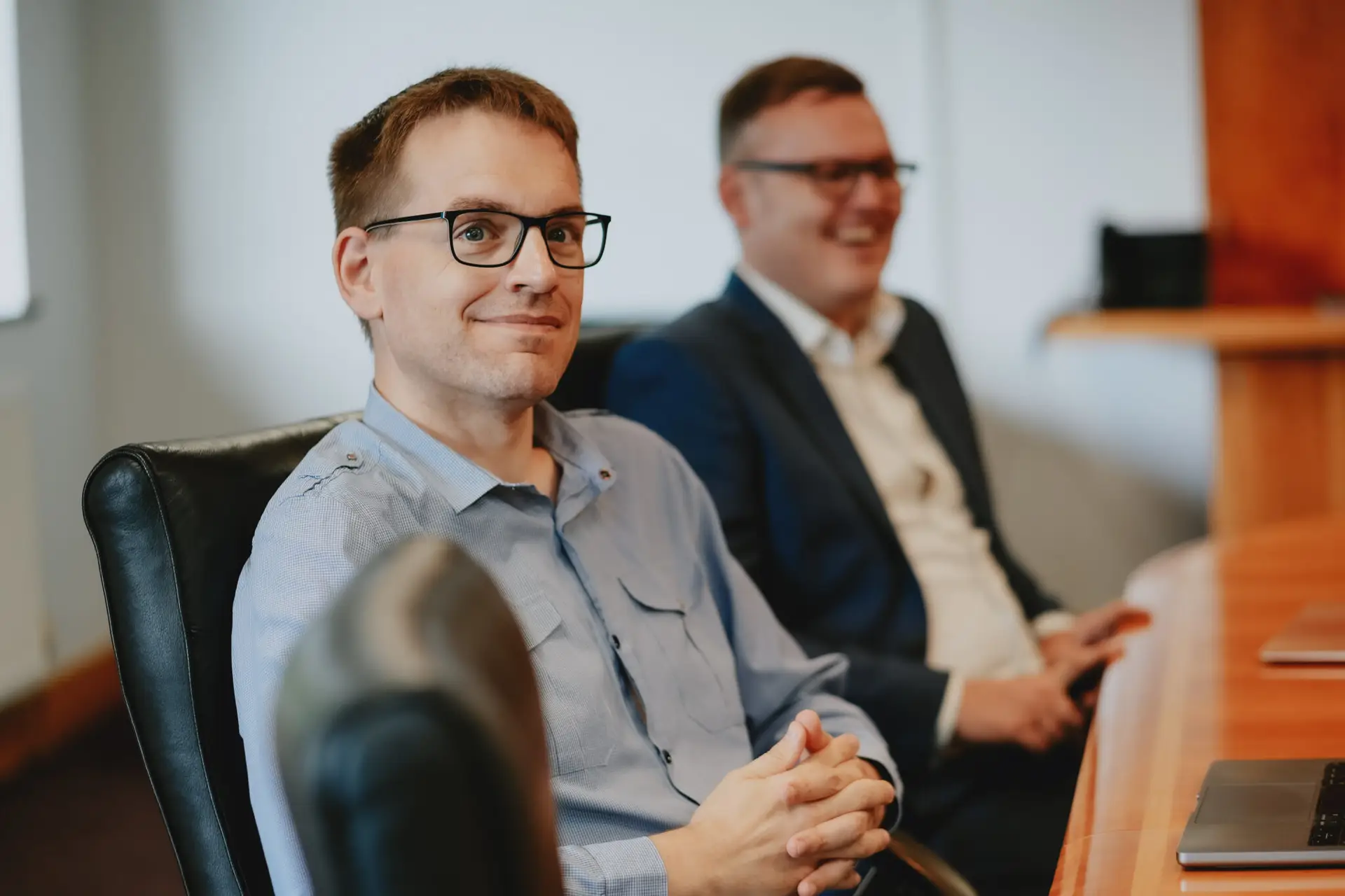 Two fogwill & jones team members sat the board room table smiling whilst listening to a speaker out of shot